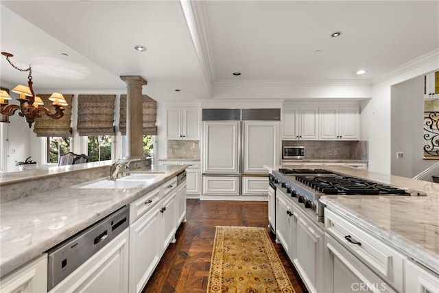 kitchen featuring a sink, a chandelier, built in appliances, white cabinetry, and light stone countertops