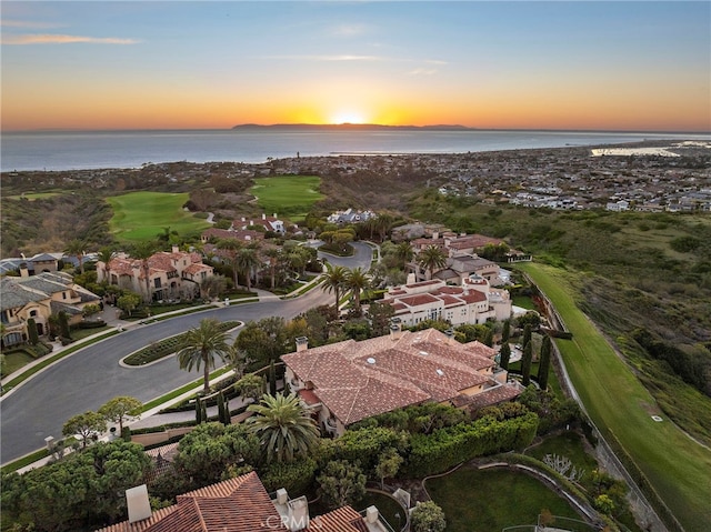 aerial view at dusk featuring view of golf course, a residential view, and a water view