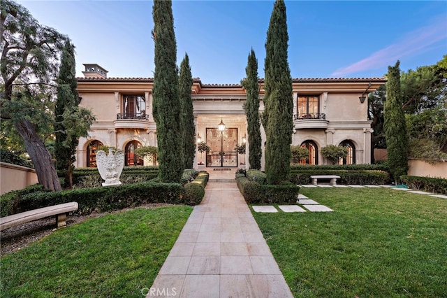 mediterranean / spanish-style home featuring stone siding, a front lawn, and a balcony