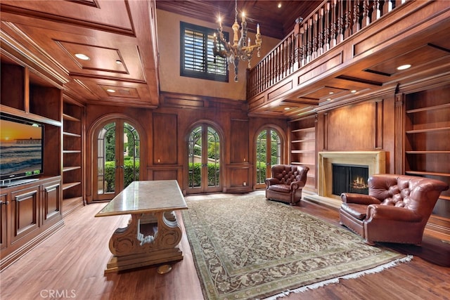 living area with wood walls, built in shelves, a notable chandelier, and french doors