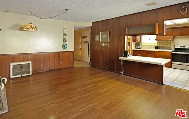 kitchen featuring hardwood / wood-style floors, wooden walls, tile counters, a textured ceiling, and stainless steel electric range