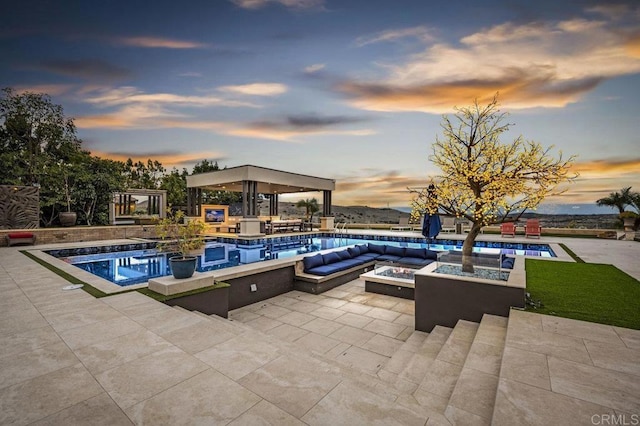 pool at dusk featuring a jacuzzi, an outdoor living space with a fire pit, and a patio