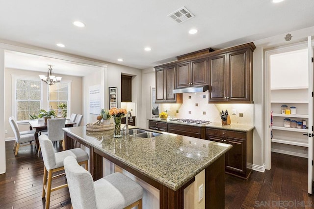 kitchen featuring an island with sink, sink, dark hardwood / wood-style flooring, light stone countertops, and dark brown cabinets