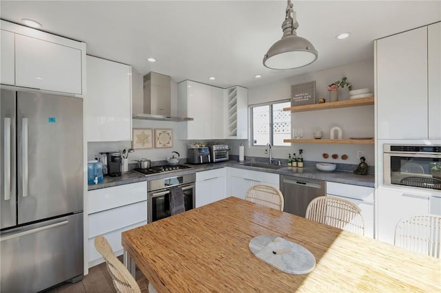 kitchen featuring wall chimney range hood, sink, appliances with stainless steel finishes, white cabinetry, and hanging light fixtures