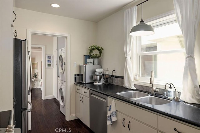 kitchen featuring stacked washing maching and dryer, appliances with stainless steel finishes, sink, white cabinets, and hanging light fixtures