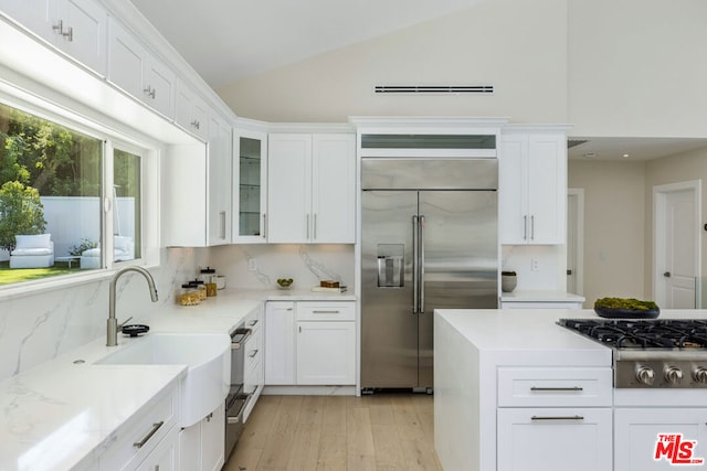 kitchen featuring appliances with stainless steel finishes, light stone countertops, light hardwood / wood-style floors, decorative backsplash, and white cabinets