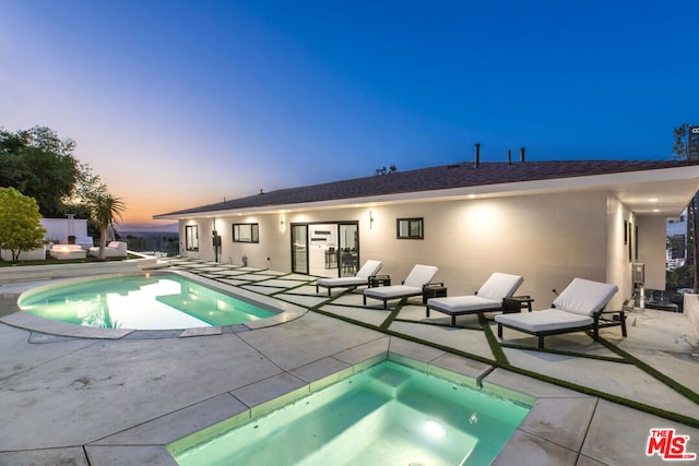 pool at dusk featuring a jacuzzi and a patio area