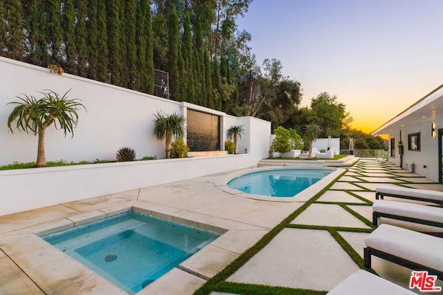 pool at dusk featuring a patio area and an in ground hot tub