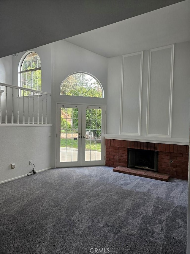 unfurnished living room featuring carpet, a towering ceiling, a fireplace, and french doors