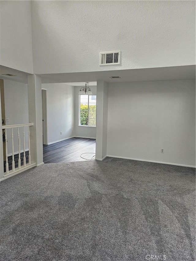 unfurnished room featuring an inviting chandelier, dark carpet, and a textured ceiling