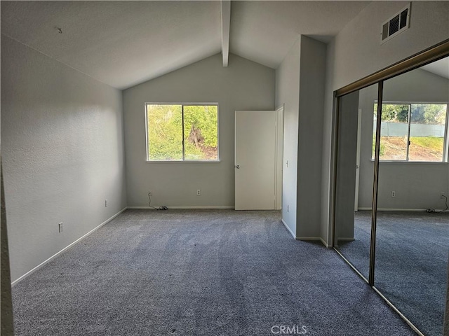 unfurnished bedroom featuring multiple windows, carpet, lofted ceiling with beams, and a closet