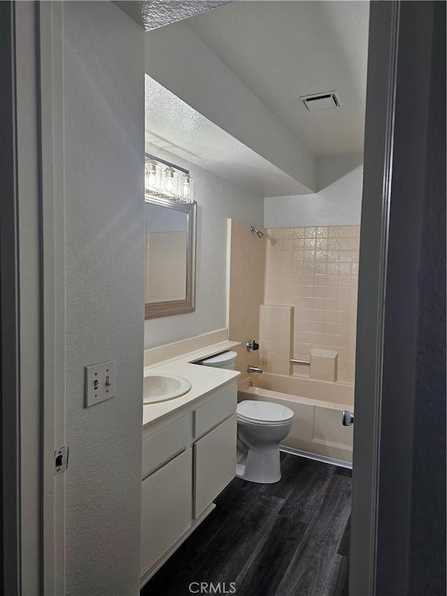 full bathroom featuring wood-type flooring, vanity,  shower combination, toilet, and a textured ceiling