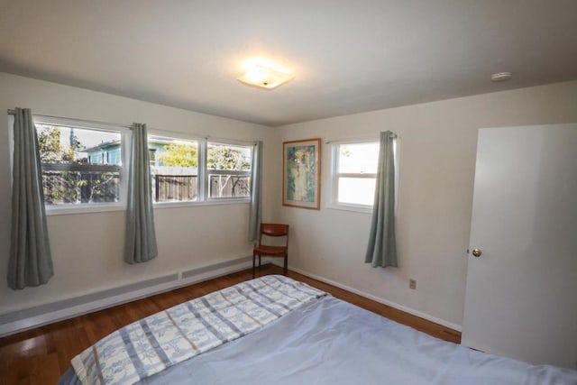 unfurnished bedroom with multiple windows, a baseboard heating unit, and dark wood-type flooring