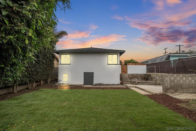 back house at dusk featuring a lawn