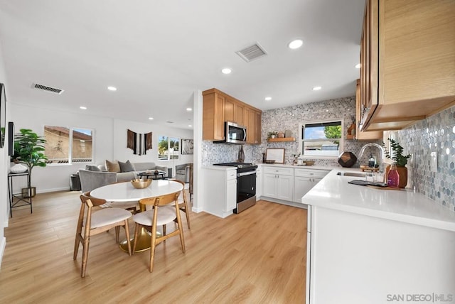 kitchen featuring sink, stainless steel appliances, tasteful backsplash, white cabinets, and light wood-type flooring