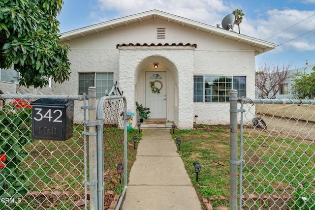 view of front of house with a front yard, a gate, fence, and stucco siding