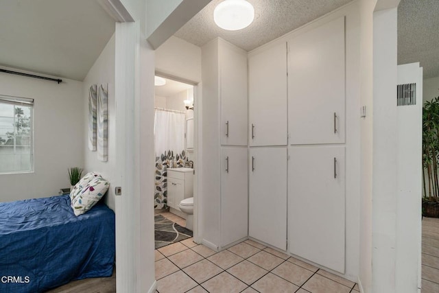 bedroom with light tile patterned floors, a textured ceiling, and connected bathroom