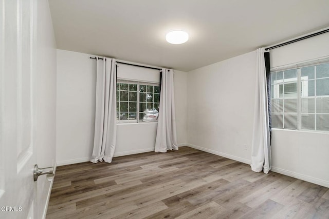 spare room featuring wood finished floors, a wealth of natural light, and baseboards