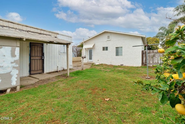 back of property with an outbuilding, a lawn, and fence