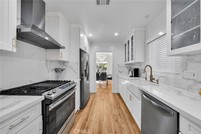 kitchen with sink, appliances with stainless steel finishes, light stone counters, white cabinets, and exhaust hood