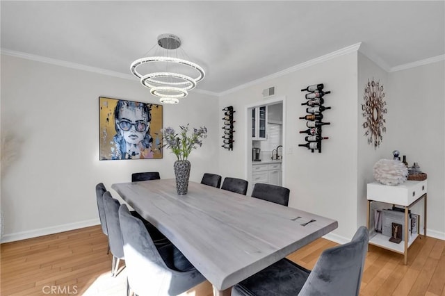 dining area with crown molding, sink, an inviting chandelier, and light hardwood / wood-style flooring