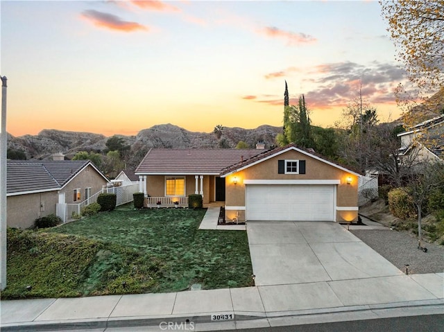 ranch-style home with an attached garage, a mountain view, driveway, a lawn, and stucco siding