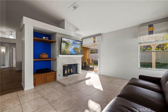 living area featuring light tile patterned floors, baseboards, visible vents, built in features, and a fireplace