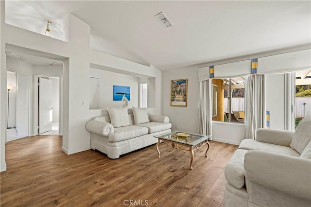 living room with vaulted ceiling, visible vents, hardwood / wood-style flooring, and baseboards