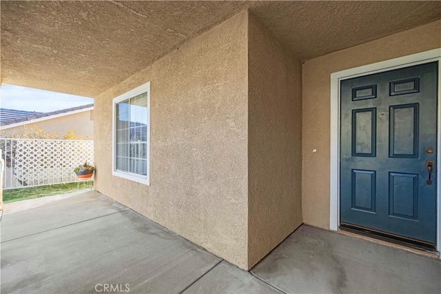 entrance to property with a patio area, fence, and stucco siding