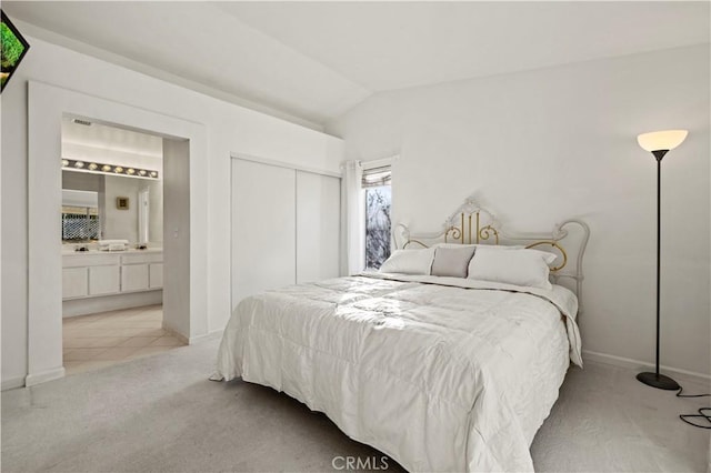 bedroom featuring a closet, light carpet, vaulted ceiling, and ensuite bath