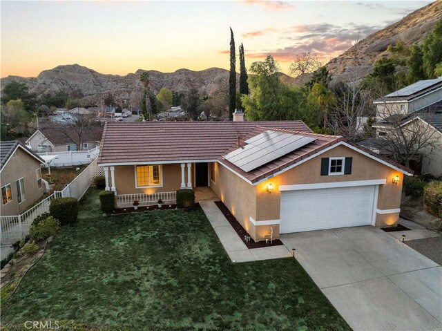 ranch-style house with a garage, a mountain view, a lawn, and solar panels