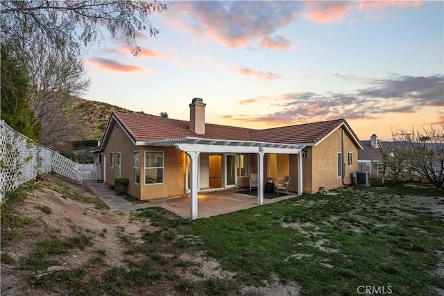 back of house at dusk with a chimney, stucco siding, a lawn, a patio area, and a fenced backyard