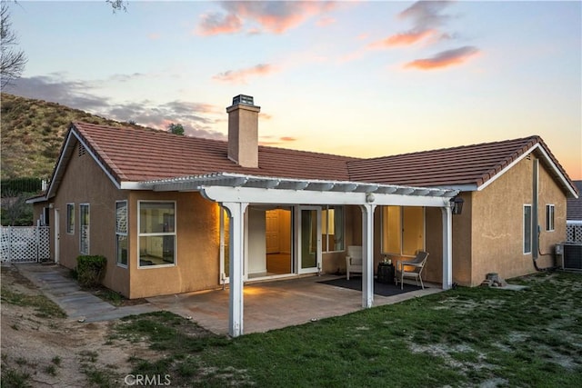 back of property at dusk featuring a pergola, a chimney, a patio area, central AC, and stucco siding