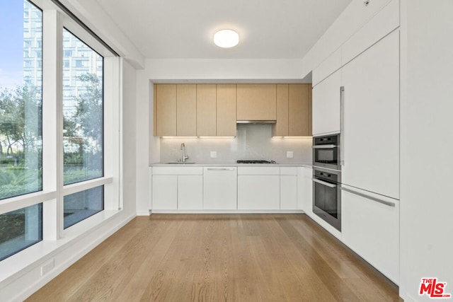 kitchen featuring sink, light hardwood / wood-style flooring, gas cooktop, dishwasher, and backsplash