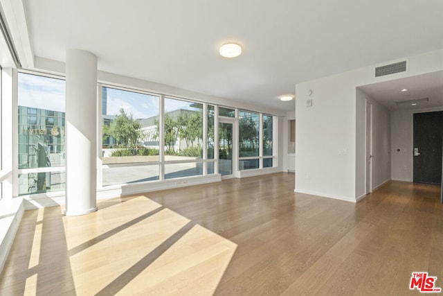 spare room with expansive windows, a healthy amount of sunlight, and hardwood / wood-style floors