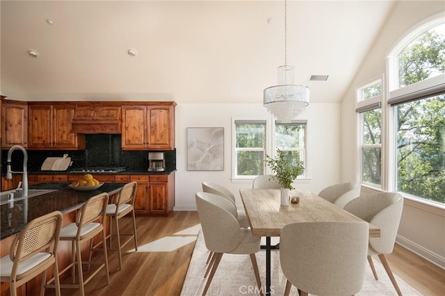 dining space with light hardwood / wood-style flooring, sink, vaulted ceiling, and a chandelier