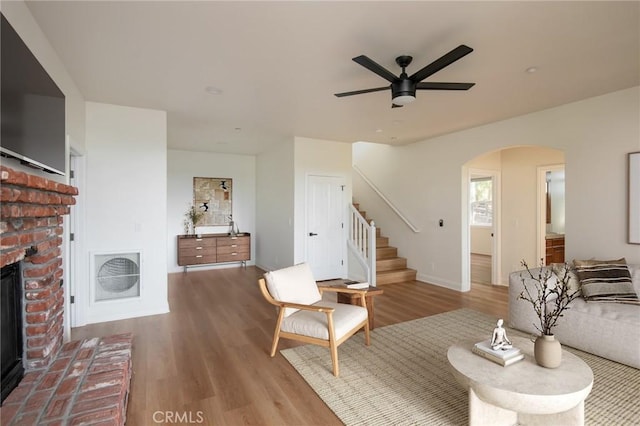 living room featuring ceiling fan, a brick fireplace, and light wood-type flooring