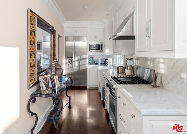 kitchen with built in appliances, white cabinets, light stone countertops, decorative backsplash, and wall chimney range hood