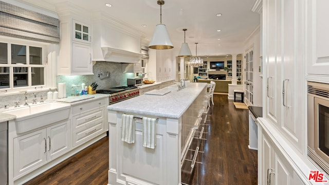 kitchen with sink, hanging light fixtures, light stone counters, white cabinets, and a center island with sink