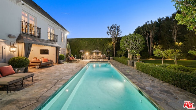 pool at dusk with a patio and an outdoor living space with a fire pit