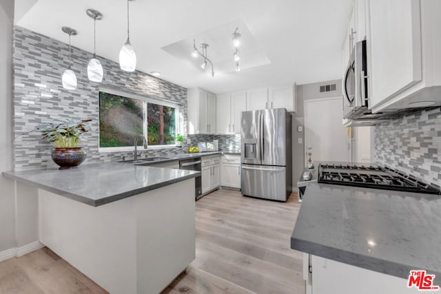 kitchen with decorative light fixtures, sink, white cabinets, kitchen peninsula, and stainless steel appliances