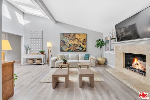 living room featuring a tiled fireplace, vaulted ceiling with skylight, and light wood-type flooring