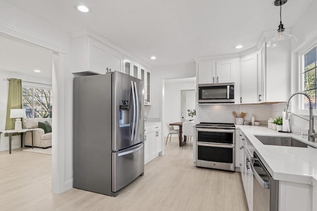 kitchen with pendant lighting, sink, stainless steel appliances, light stone countertops, and white cabinets