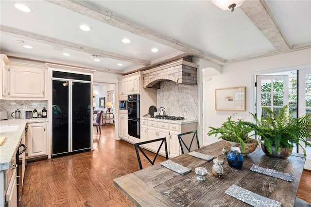 kitchen with tasteful backsplash, dark hardwood / wood-style floors, beamed ceiling, light stone countertops, and black appliances