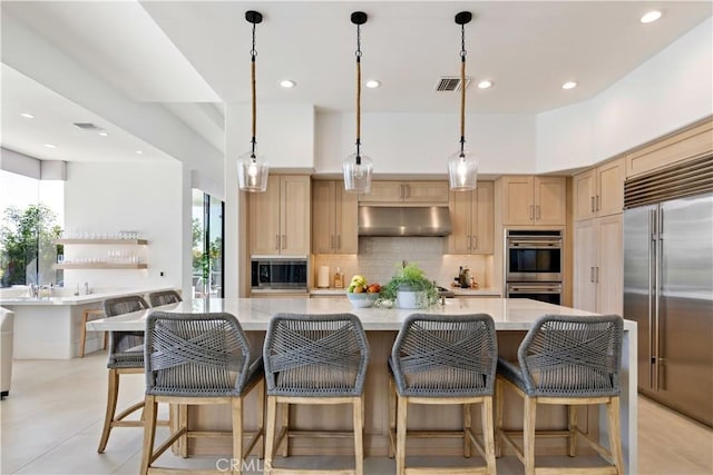 kitchen featuring a spacious island, built in appliances, a breakfast bar area, and light brown cabinets