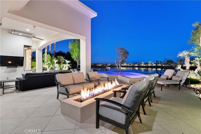 patio at twilight featuring a water view, ceiling fan, and an outdoor living space with a fire pit