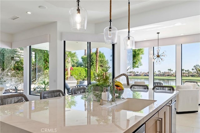 kitchen featuring pendant lighting, sink, a water view, light stone counters, and a chandelier