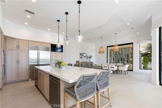 kitchen featuring sink, a kitchen breakfast bar, hanging light fixtures, a large island, and light stone countertops