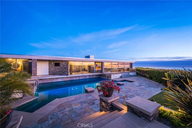 pool at dusk with a hot tub and a patio