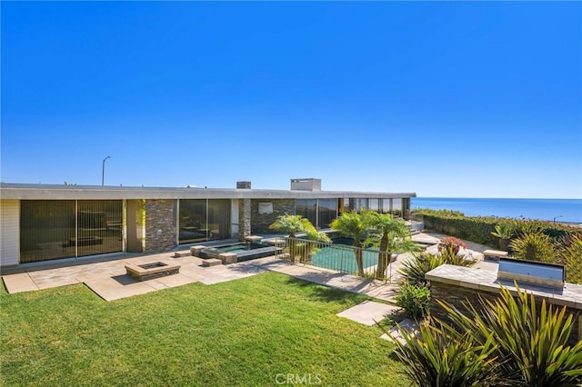 rear view of property with a patio, a water view, a yard, and a fire pit